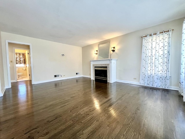 unfurnished living room with visible vents, dark wood finished floors, baseboards, and a fireplace