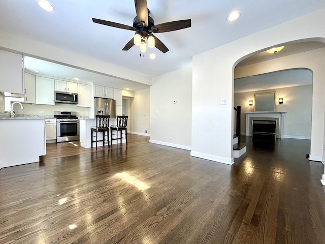 living area featuring a ceiling fan, arched walkways, baseboards, recessed lighting, and dark wood-type flooring