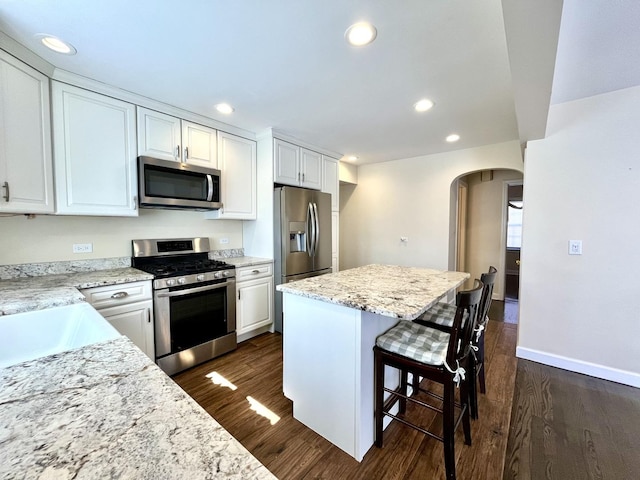 kitchen featuring arched walkways, a kitchen breakfast bar, dark wood-style floors, and stainless steel appliances