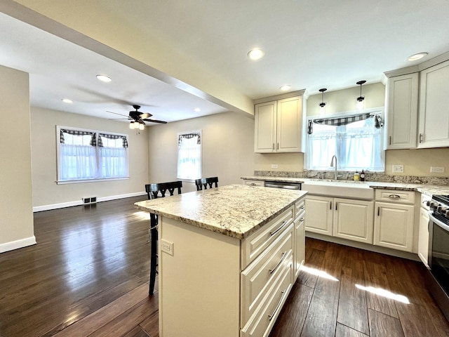 kitchen featuring dark wood-type flooring, a sink, a breakfast bar area, and light stone countertops