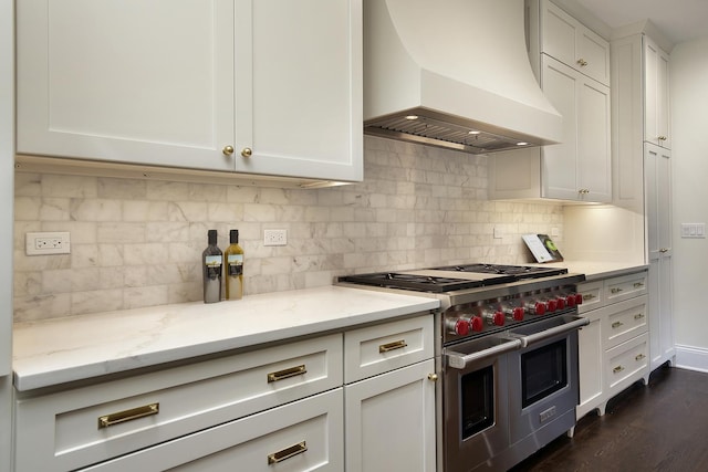 kitchen with white cabinets, range with two ovens, light stone counters, and custom exhaust hood