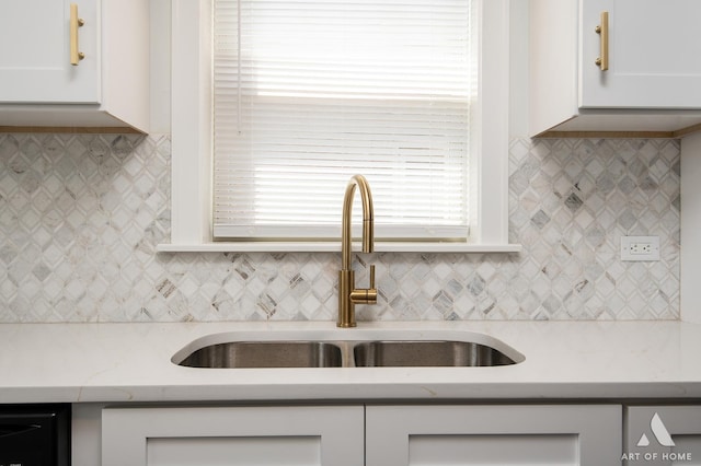 kitchen with backsplash, white cabinets, light stone counters, and a sink