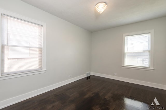 spare room with baseboards, dark wood-style flooring, and visible vents