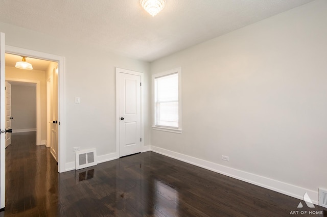 unfurnished bedroom with a closet, baseboards, dark wood-type flooring, and visible vents