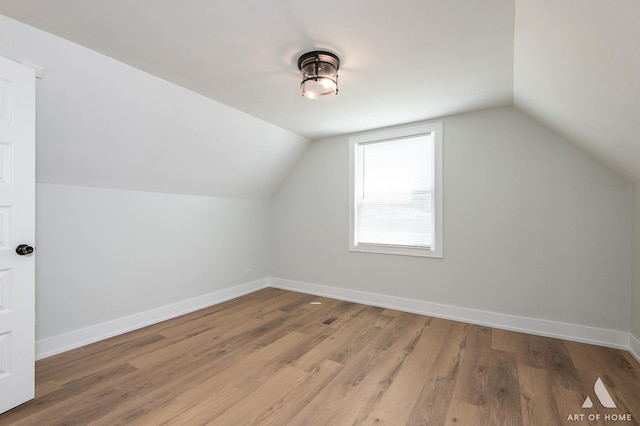 additional living space with baseboards, light wood-style flooring, and vaulted ceiling