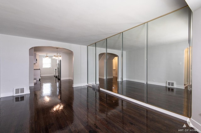 spare room with arched walkways, visible vents, and wood finished floors