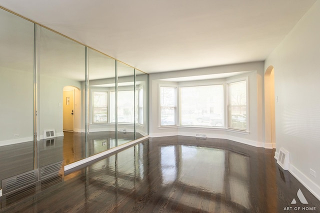 empty room featuring visible vents, arched walkways, baseboards, and wood finished floors