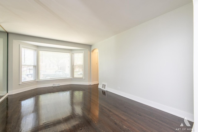 unfurnished room featuring baseboards, arched walkways, dark wood finished floors, and visible vents