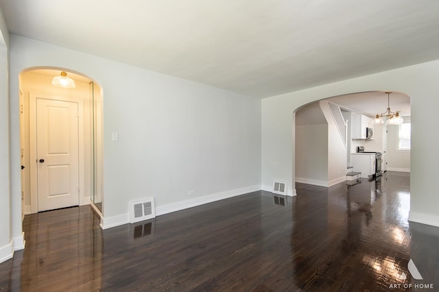 unfurnished living room with arched walkways, visible vents, and dark wood-type flooring