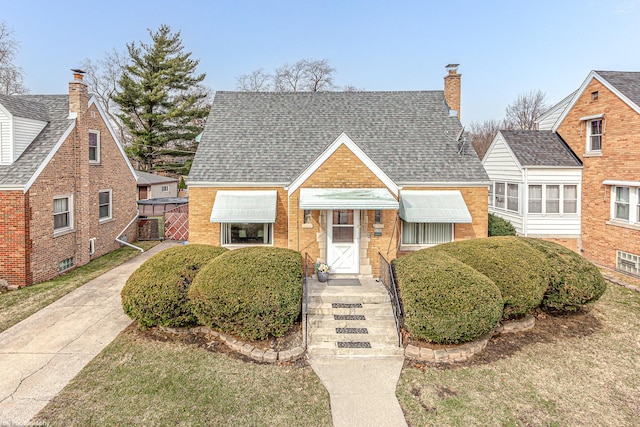 view of front of home featuring brick siding, a shingled roof, and a chimney