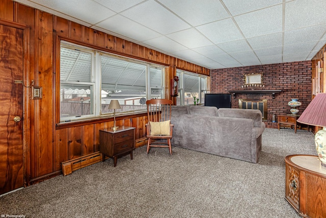 carpeted living area featuring wood walls, a brick fireplace, a drop ceiling, and baseboard heating