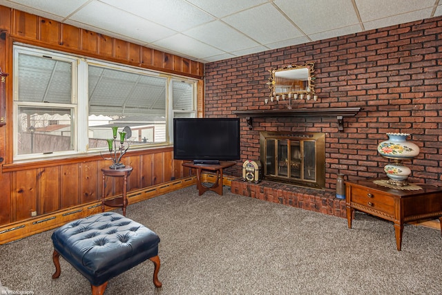 carpeted living room with wooden walls, a brick fireplace, and a drop ceiling