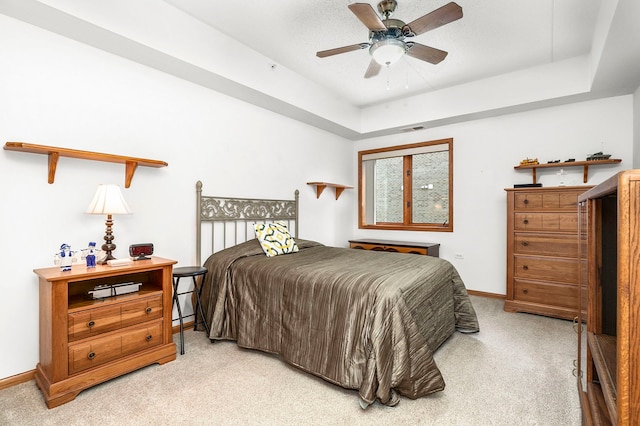 bedroom with a ceiling fan, visible vents, light colored carpet, baseboards, and a raised ceiling
