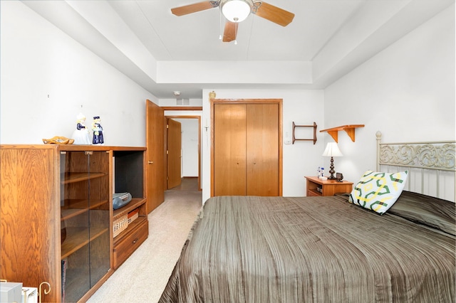 carpeted bedroom featuring a raised ceiling, ceiling fan, and a closet
