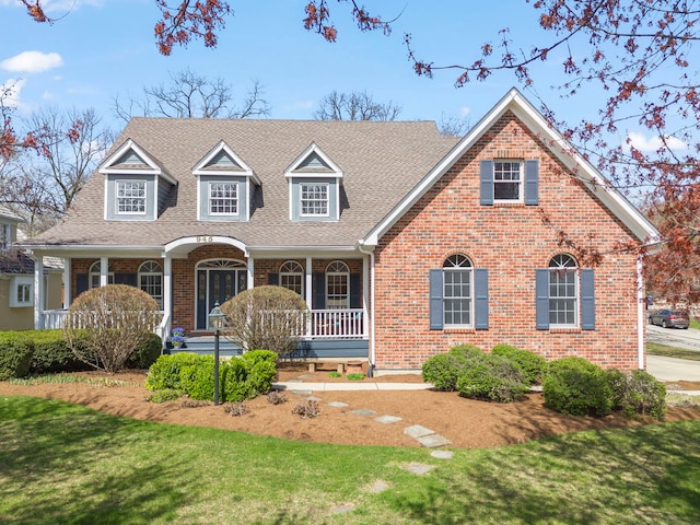 cape cod house featuring roof with shingles, a front yard, a porch, and brick siding