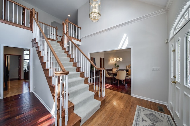 foyer entrance with visible vents, wood finished floors, stairway, an inviting chandelier, and a high ceiling
