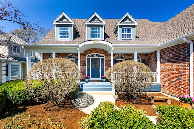 view of front of house with a shingled roof, a porch, and brick siding