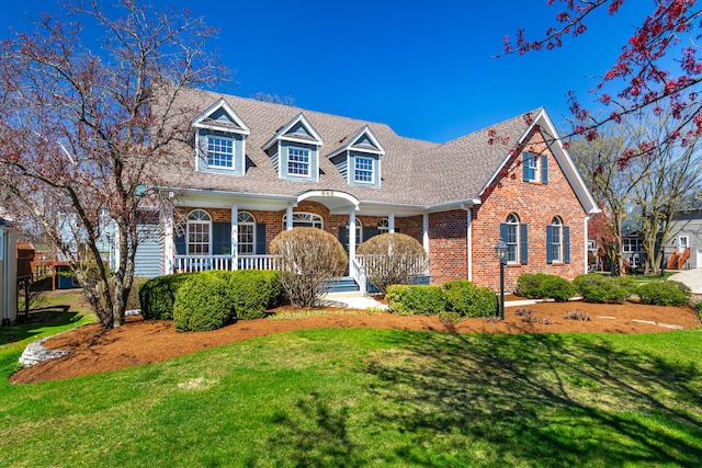 cape cod house with brick siding, covered porch, and a front yard