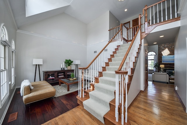 stairway with baseboards, a towering ceiling, hardwood / wood-style floors, and a large fireplace