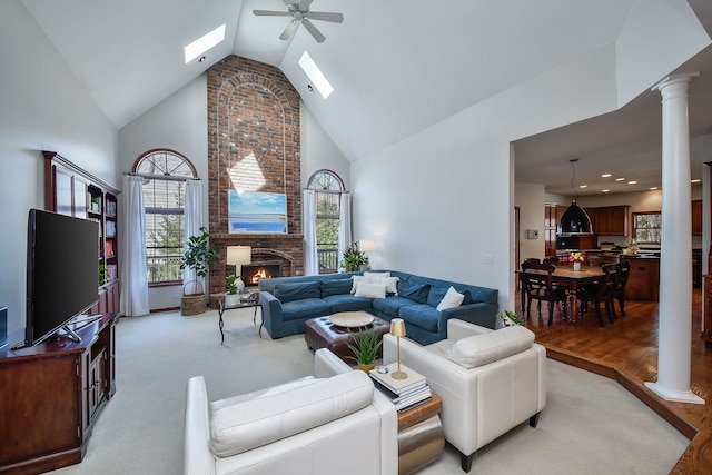 living room with a brick fireplace, high vaulted ceiling, ornate columns, a ceiling fan, and a skylight