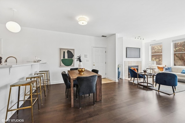 dining area featuring a tiled fireplace, baseboards, dark wood finished floors, and visible vents