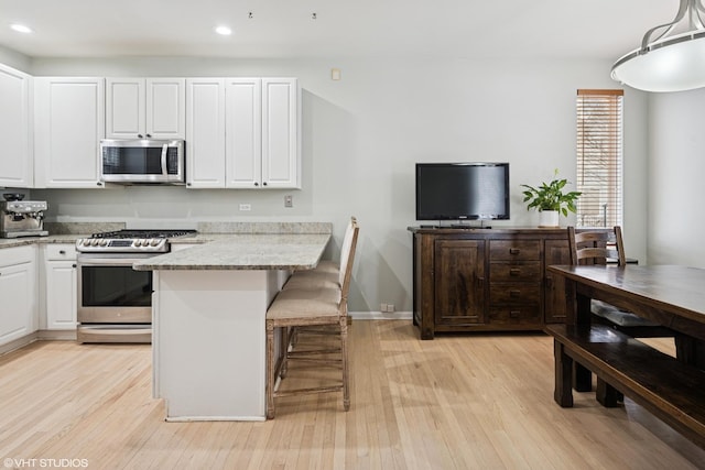 kitchen featuring light wood-style flooring, stainless steel appliances, recessed lighting, white cabinetry, and a kitchen bar