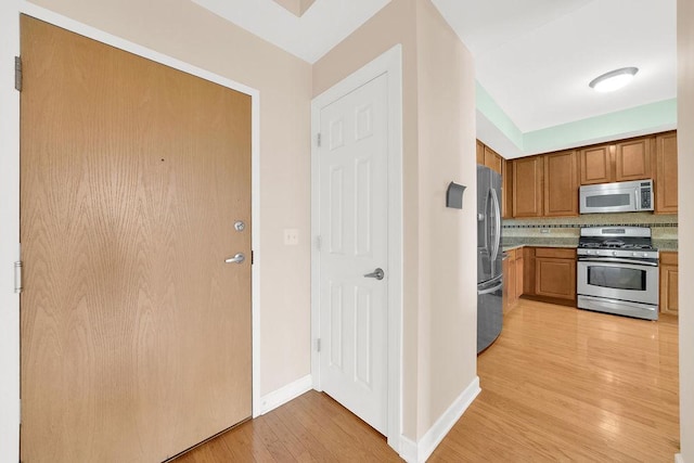 kitchen with brown cabinetry, decorative backsplash, baseboards, light wood-type flooring, and appliances with stainless steel finishes