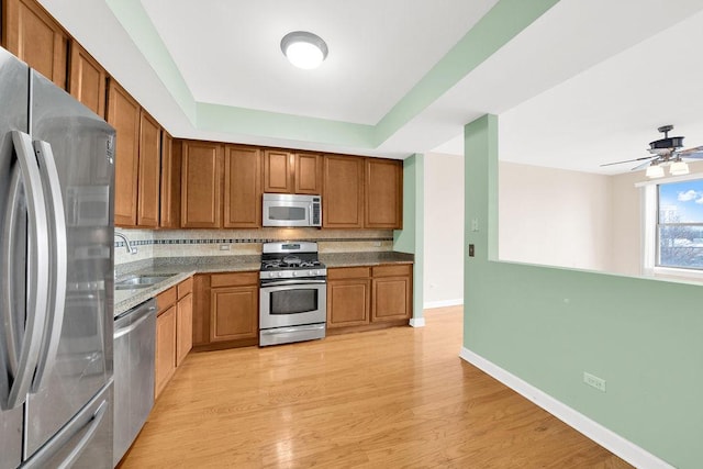 kitchen featuring decorative backsplash, brown cabinets, a sink, light wood finished floors, and stainless steel appliances