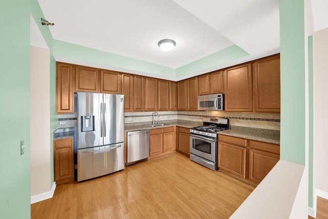 kitchen with brown cabinetry, tasteful backsplash, a sink, light wood-style flooring, and stainless steel appliances