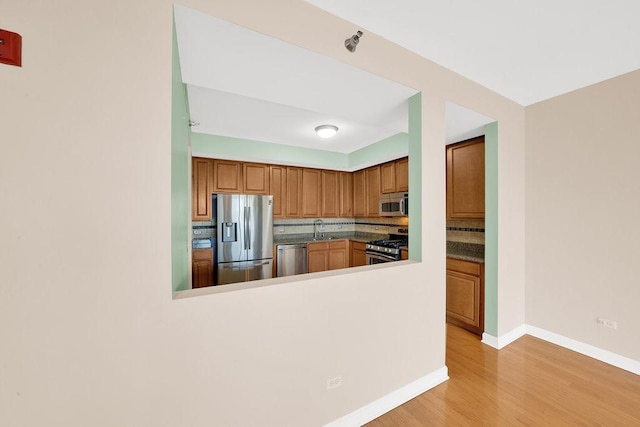 kitchen featuring decorative backsplash, light wood-style floors, baseboards, a sink, and appliances with stainless steel finishes