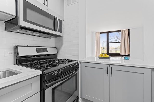kitchen featuring light stone counters, gray cabinets, stainless steel appliances, decorative backsplash, and visible vents