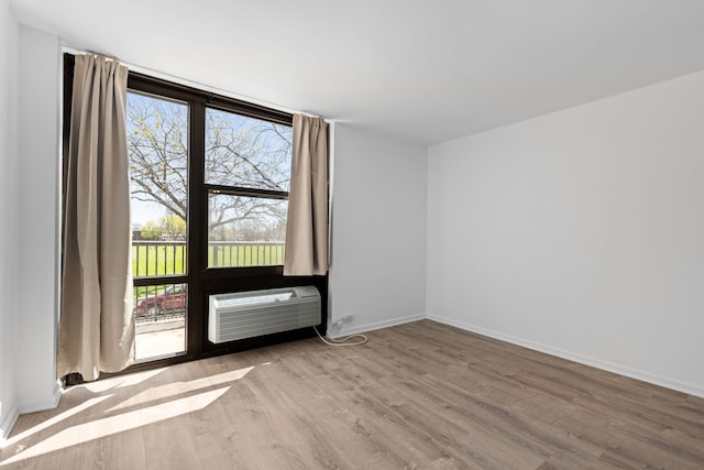 spare room with baseboards, a wall unit AC, and wood finished floors