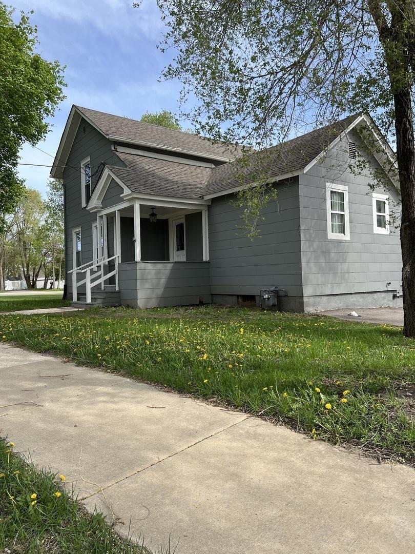 view of side of home with roof with shingles, covered porch, and a yard