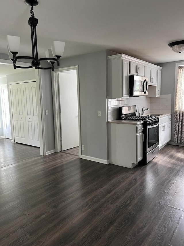 kitchen with an inviting chandelier, dark wood-style flooring, white cabinets, appliances with stainless steel finishes, and backsplash