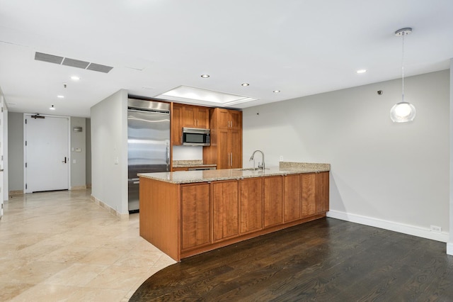 kitchen with brown cabinetry, a peninsula, light stone counters, a sink, and stainless steel appliances