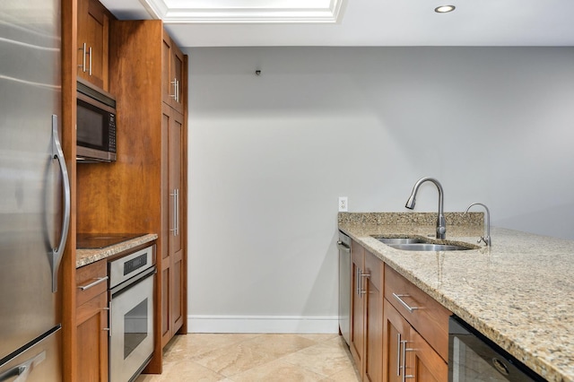 kitchen featuring a sink, brown cabinets, black appliances, and light stone countertops