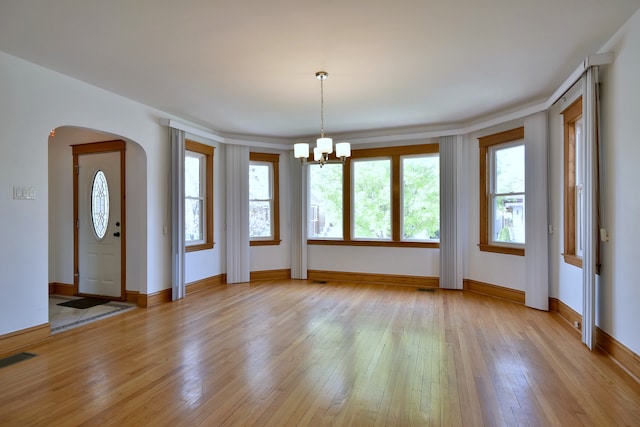 7840 W Cressett Dr, Elmwood Park, IL 60707 - unfurnished dining area with a chandelier, light wood-type flooring, arched walkways, and baseboards