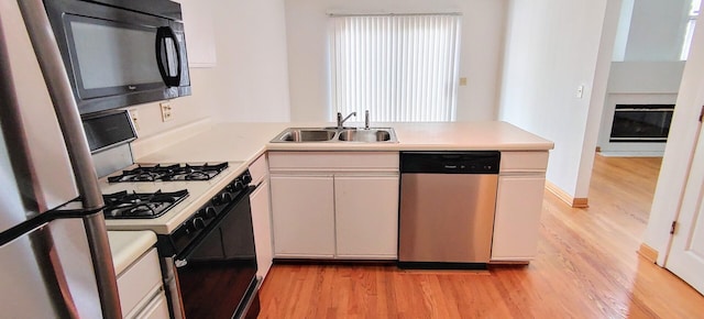 kitchen with a peninsula, light wood-style floors, light countertops, a sink, and appliances with stainless steel finishes