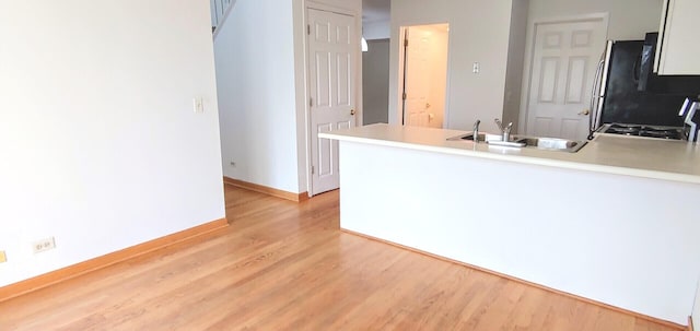 kitchen with a peninsula, light wood-type flooring, light countertops, a sink, and gas stove