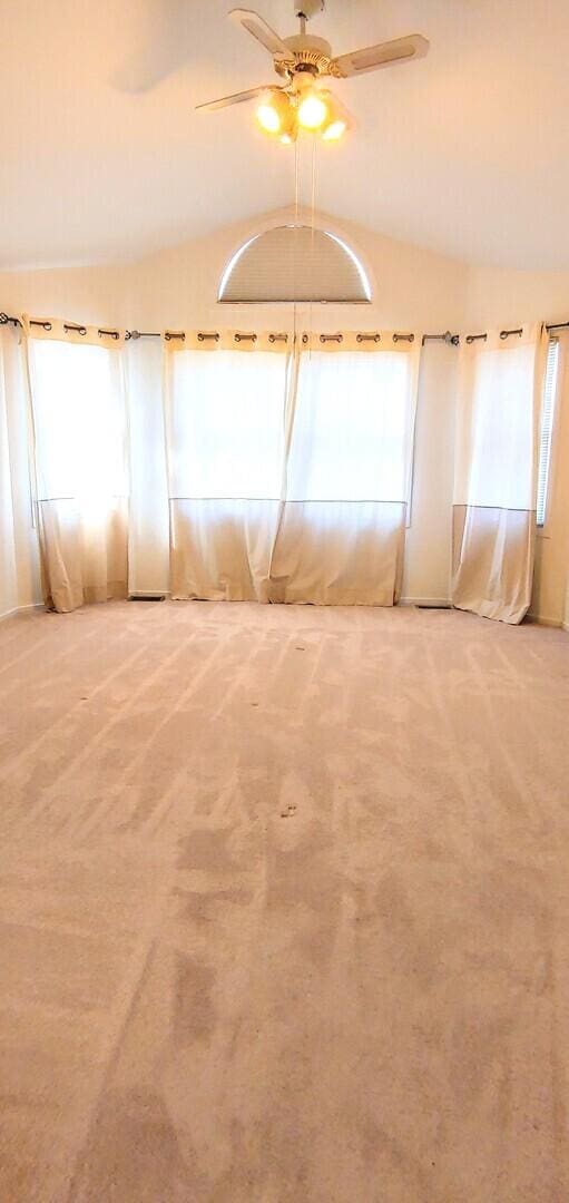empty room featuring a healthy amount of sunlight, ceiling fan, carpet, and vaulted ceiling