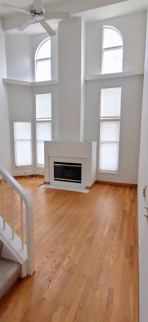 unfurnished living room featuring ceiling fan, a glass covered fireplace, plenty of natural light, and wood finished floors
