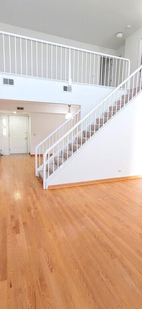 unfurnished living room with stairs, a high ceiling, visible vents, and wood finished floors