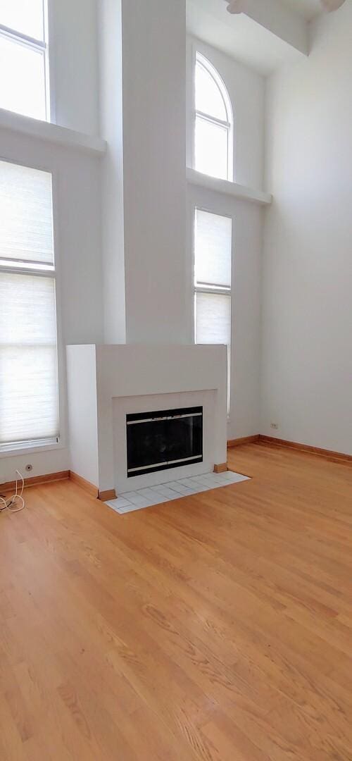 unfurnished living room featuring baseboards, a fireplace with flush hearth, and wood finished floors