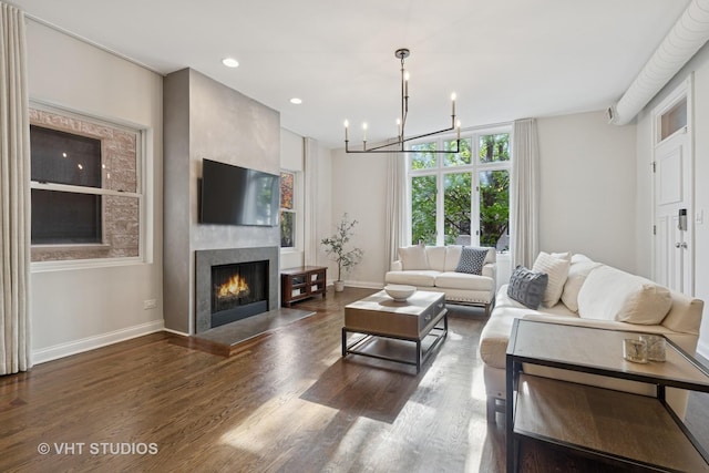 living area with wood finished floors, baseboards, a lit fireplace, recessed lighting, and a notable chandelier