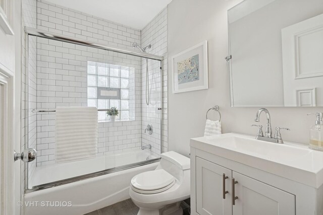 full bath featuring vanity, toilet, and shower / bath combination with glass door