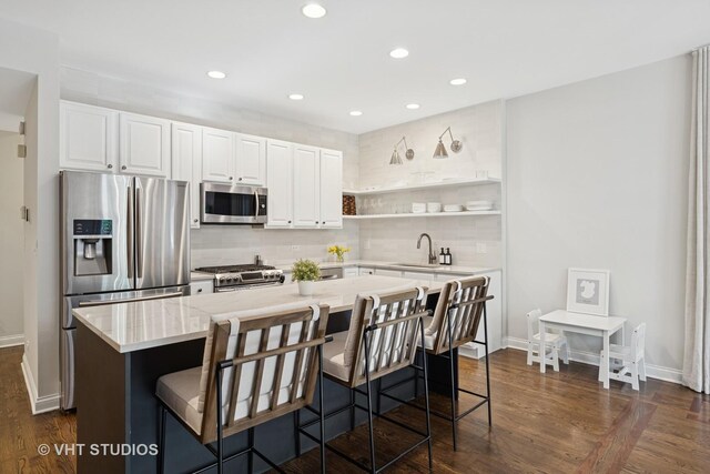 kitchen featuring a kitchen island, tasteful backsplash, baseboards, stainless steel appliances, and white cabinetry