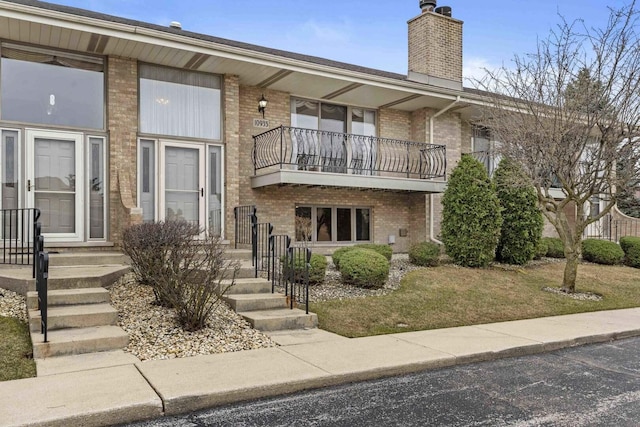 view of front facade featuring brick siding, a front lawn, a balcony, and a chimney
