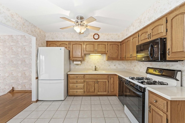 kitchen featuring ceiling fan, wallpapered walls, a sink, light tile patterned floors, and black appliances