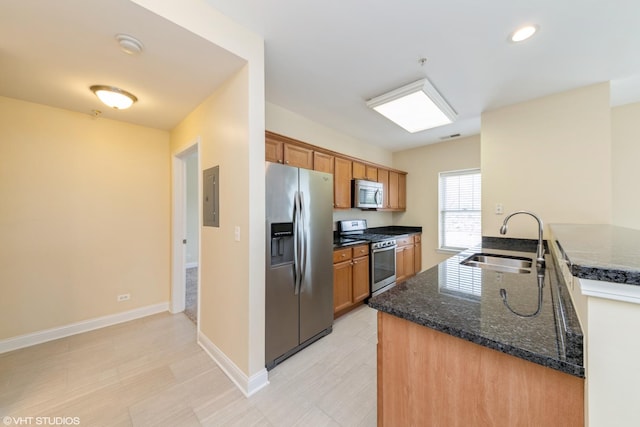 kitchen with electric panel, brown cabinetry, appliances with stainless steel finishes, a sink, and baseboards