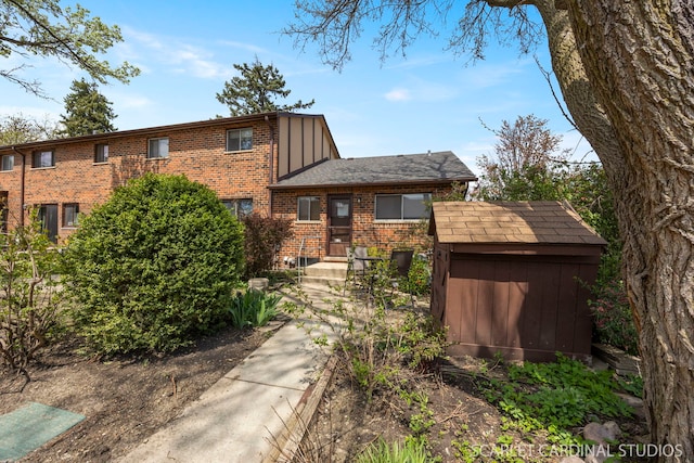 view of front facade with a storage shed, brick siding, board and batten siding, and an outdoor structure